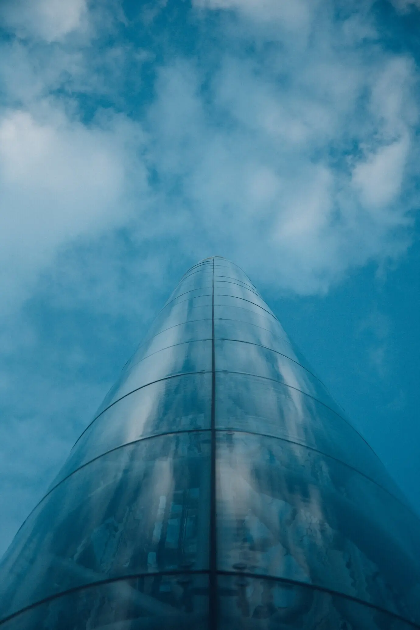 A low-angle view of a tower in Oslo, Norway, mirroring the cloudy blue sky.